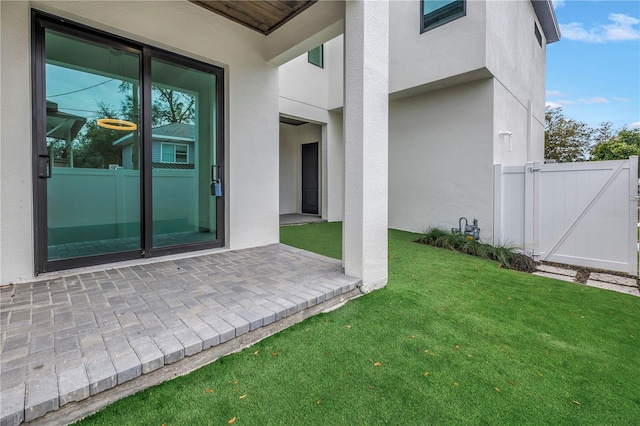 property entrance featuring a lawn, a gate, fence, a patio area, and stucco siding