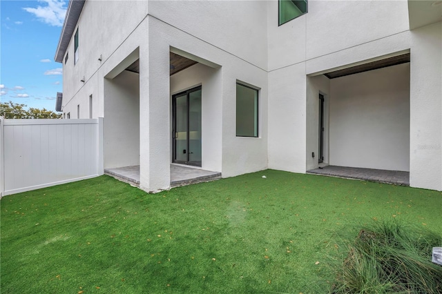 rear view of property featuring a lawn, a patio area, fence, and stucco siding