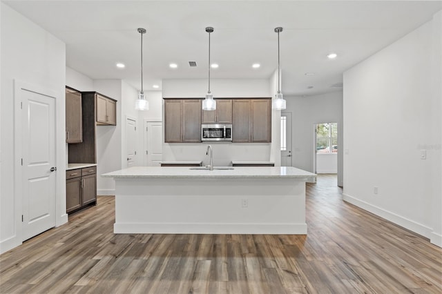 kitchen featuring hanging light fixtures, a center island with sink, stainless steel microwave, and a sink