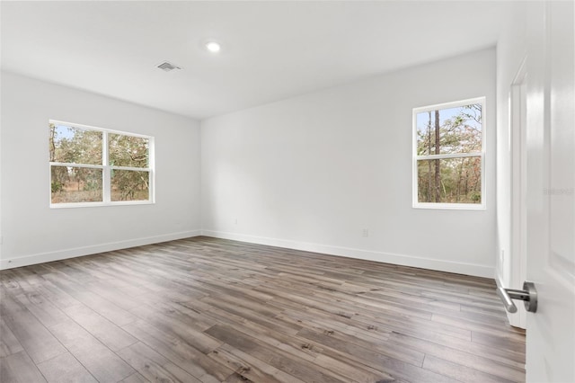 empty room featuring baseboards, plenty of natural light, visible vents, and wood finished floors