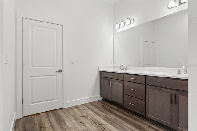 full bath with a sink, double vanity, wood finished floors, and baseboards