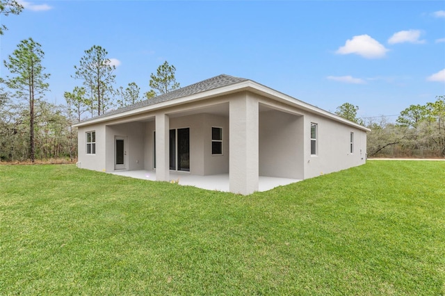 back of property featuring a yard, roof with shingles, stucco siding, and a patio