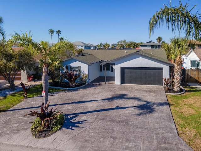 ranch-style house with decorative driveway, fence, an attached garage, and stucco siding