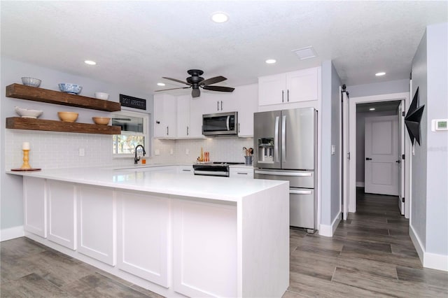 kitchen with a peninsula, open shelves, stainless steel appliances, white cabinets, and a barn door