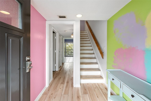 interior space with stairway, light wood-style flooring, visible vents, and baseboards