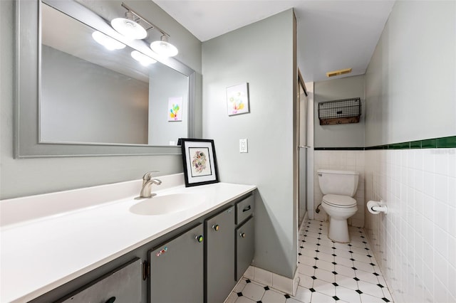 bathroom with tile walls, toilet, wainscoting, vanity, and tile patterned floors