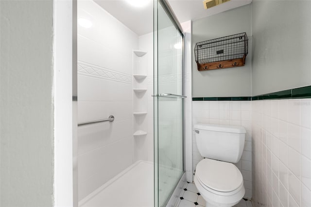 bathroom with toilet, a wainscoted wall, visible vents, tile walls, and a shower stall