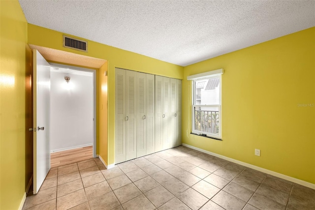 unfurnished bedroom with a closet, visible vents, light tile patterned flooring, a textured ceiling, and baseboards