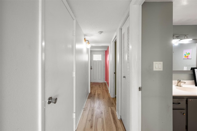 hallway featuring a textured ceiling, a sink, and light wood-style floors