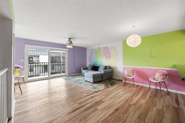 living area with a ceiling fan, baseboards, light wood-style flooring, and a textured ceiling