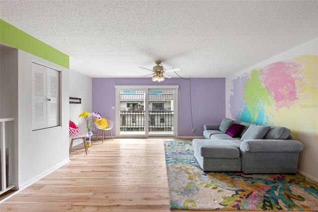 living area with light wood finished floors, ceiling fan, baseboards, and a textured ceiling