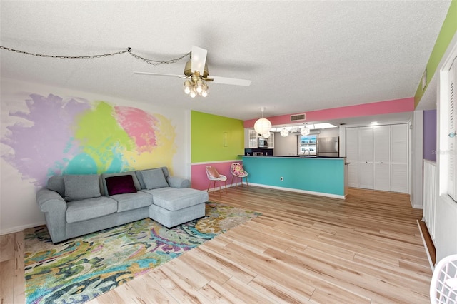 living area featuring visible vents, baseboards, ceiling fan, a textured ceiling, and light wood-style floors