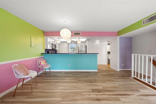 kitchen with a peninsula, visible vents, appliances with stainless steel finishes, dark countertops, and decorative light fixtures