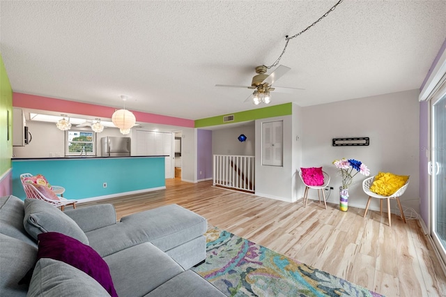 living area featuring visible vents, light wood-style flooring, a ceiling fan, a textured ceiling, and baseboards