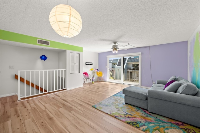 living room featuring visible vents, ceiling fan, a textured ceiling, wood finished floors, and baseboards