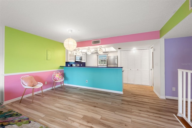 kitchen with dark countertops, decorative light fixtures, a peninsula, stainless steel appliances, and light wood-style floors