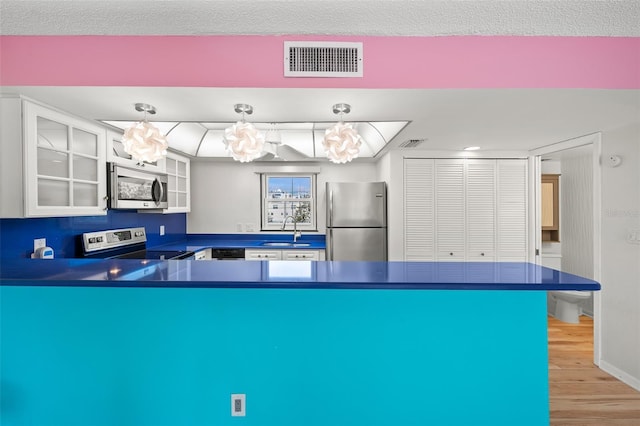 kitchen with visible vents, hanging light fixtures, appliances with stainless steel finishes, dark countertops, and glass insert cabinets