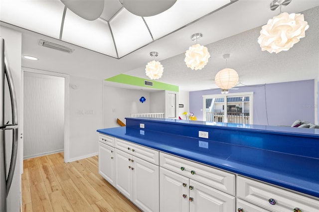 kitchen featuring pendant lighting, dark countertops, light wood-style floors, freestanding refrigerator, and white cabinets