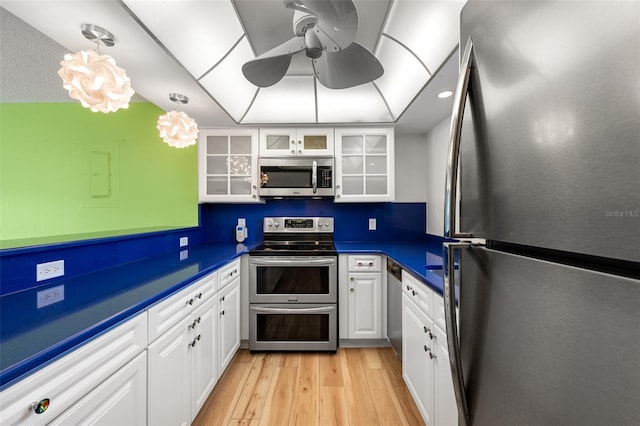 kitchen with light wood finished floors, white cabinets, dark countertops, glass insert cabinets, and stainless steel appliances