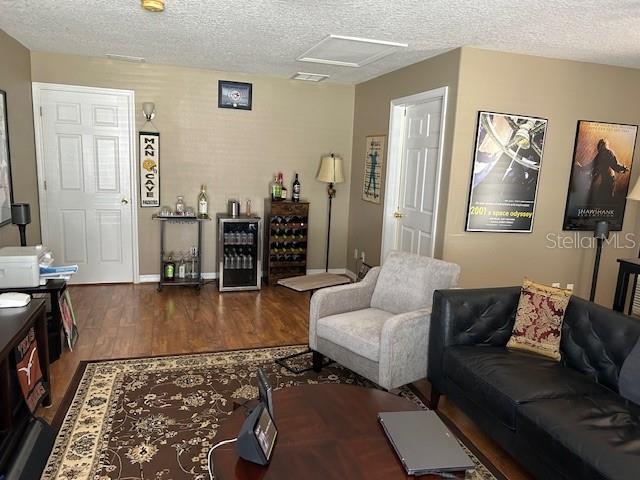 living room with attic access, a textured ceiling, wood finished floors, beverage cooler, and baseboards