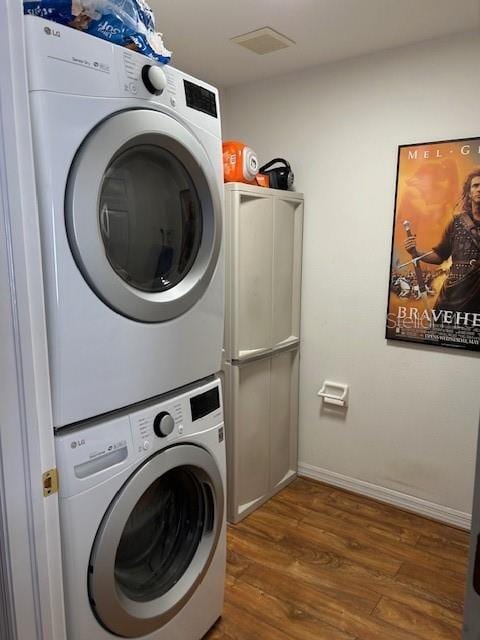 washroom with laundry area, visible vents, baseboards, stacked washer / drying machine, and wood finished floors