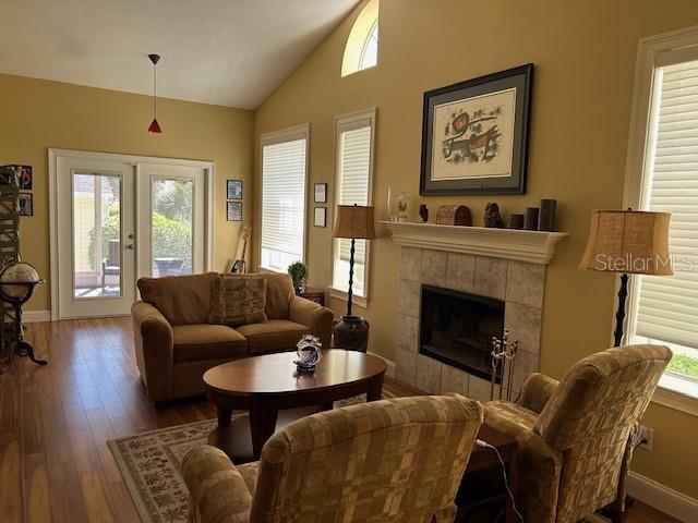 living room with wood finished floors, baseboards, vaulted ceiling, french doors, and a tiled fireplace