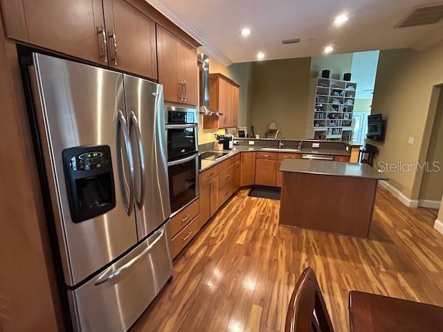 kitchen featuring light wood finished floors, a peninsula, appliances with stainless steel finishes, and visible vents