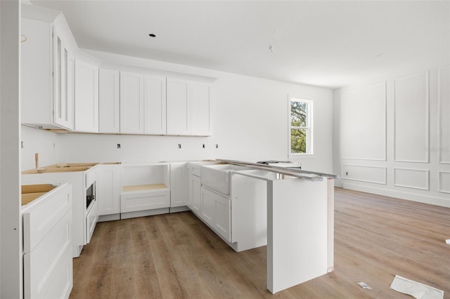 kitchen featuring light wood finished floors, white cabinetry, and a decorative wall