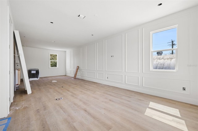 empty room with heating unit, light wood-style flooring, and a decorative wall