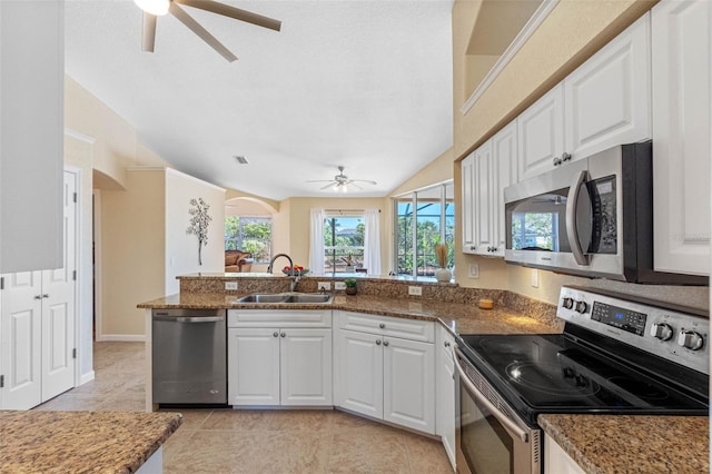 kitchen featuring appliances with stainless steel finishes, white cabinetry, a sink, dark stone counters, and a peninsula