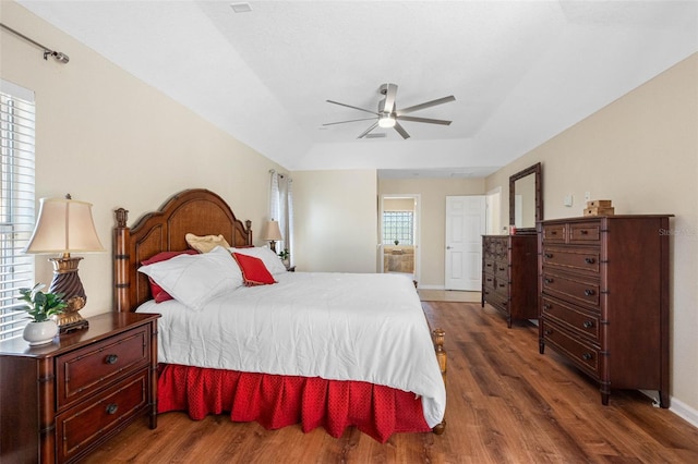 bedroom featuring a tray ceiling, wood finished floors, a ceiling fan, and baseboards