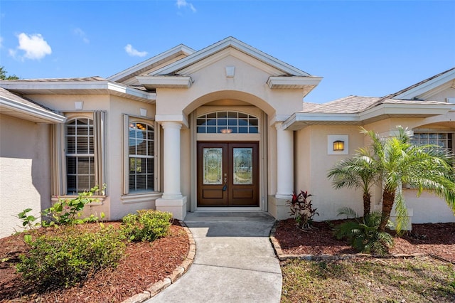 view of exterior entry with french doors, a shingled roof, and stucco siding