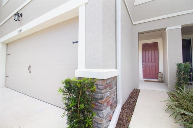 doorway to property featuring a garage, stone siding, and stucco siding