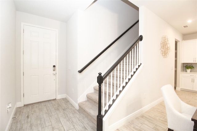 foyer featuring wood finish floors, visible vents, baseboards, and stairs