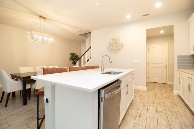 kitchen with visible vents, white cabinets, wood tiled floor, stainless steel dishwasher, and a sink