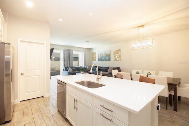 kitchen featuring appliances with stainless steel finishes, open floor plan, a kitchen island with sink, white cabinets, and a sink