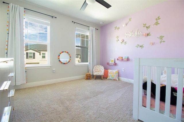 carpeted bedroom featuring a nursery area, baseboards, and a ceiling fan