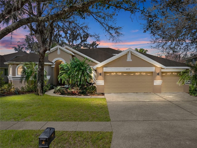 view of front facade featuring driveway, a lawn, an attached garage, and stucco siding