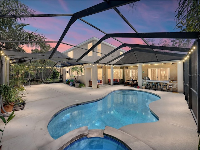 pool at dusk with outdoor dry bar, a patio area, a lanai, and a pool with connected hot tub