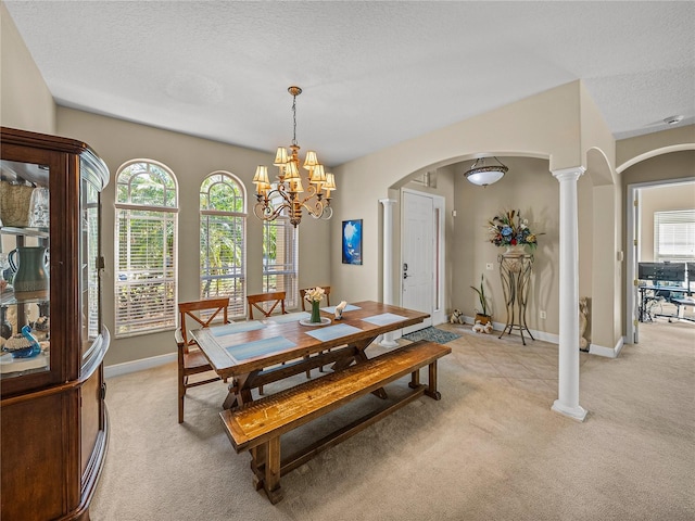 dining room with ornate columns, a textured ceiling, arched walkways, and light colored carpet