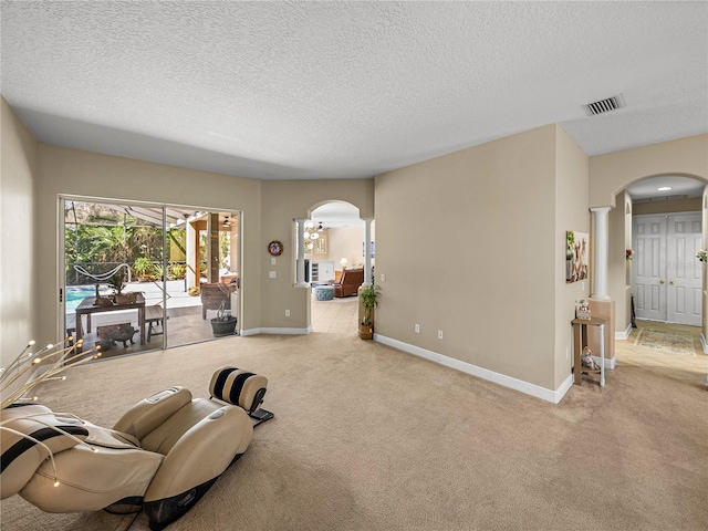 carpeted living area featuring decorative columns, visible vents, arched walkways, baseboards, and a textured ceiling