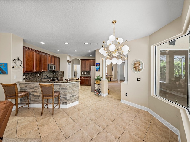 kitchen with arched walkways, light tile patterned floors, tasteful backsplash, appliances with stainless steel finishes, and a peninsula