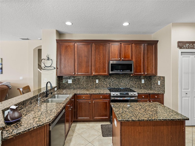 kitchen with light tile patterned floors, dark stone countertops, stainless steel appliances, and a sink