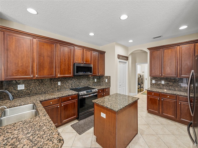 kitchen featuring light tile patterned floors, appliances with stainless steel finishes, arched walkways, and a sink