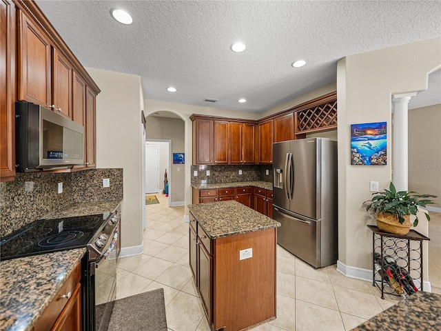 kitchen featuring arched walkways, light tile patterned floors, stainless steel appliances, a center island, and dark stone counters