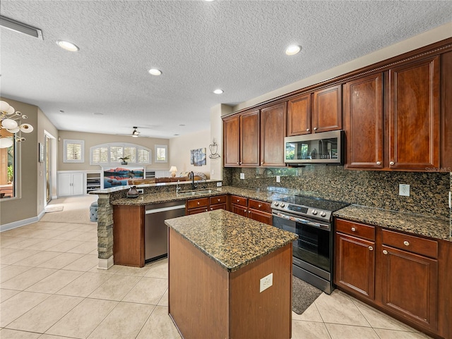 kitchen featuring a sink, open floor plan, appliances with stainless steel finishes, a center island, and dark stone countertops