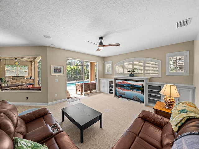 living room featuring carpet floors, ceiling fan, visible vents, and a textured ceiling