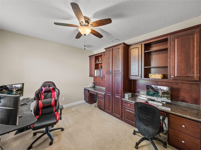 office featuring baseboards, a ceiling fan, light colored carpet, a textured ceiling, and built in desk