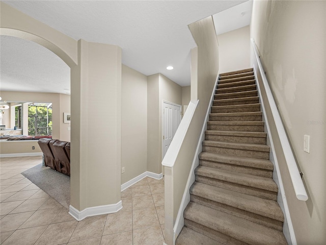 stairs with arched walkways, a textured ceiling, tile patterned flooring, and baseboards