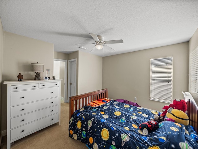 bedroom with a ceiling fan, visible vents, a textured ceiling, and light colored carpet